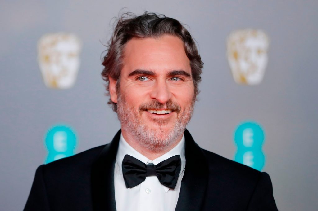 Joaquin Phoenix smiles as he wears a suit and bow tie on a BAFTA red carpet event.