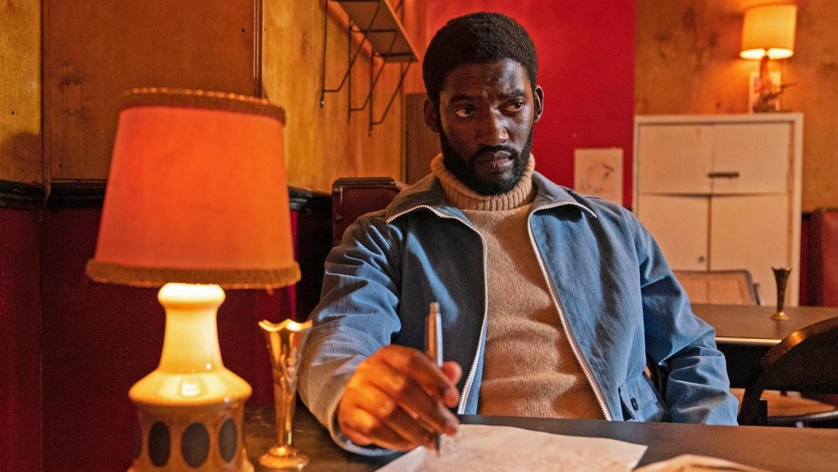 Malachi Kirby as Darcus Howe does work at a table as seen in Steve McQueen's Small Axe Anthology.