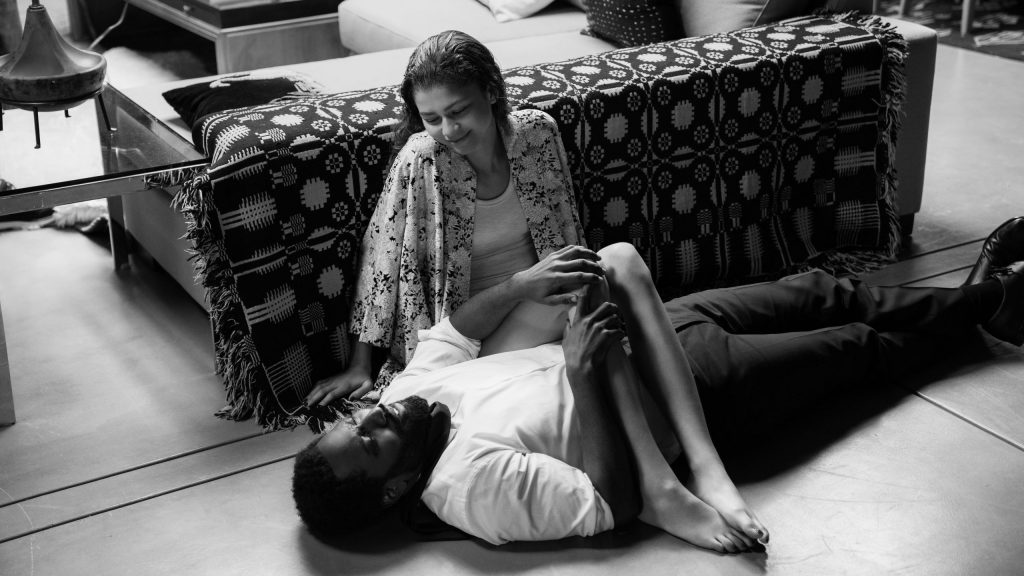 Zendaya and John David Washington sit carelessly on the floor together in their modern living room as seen in the black-and-white film Malcolm & Marie.