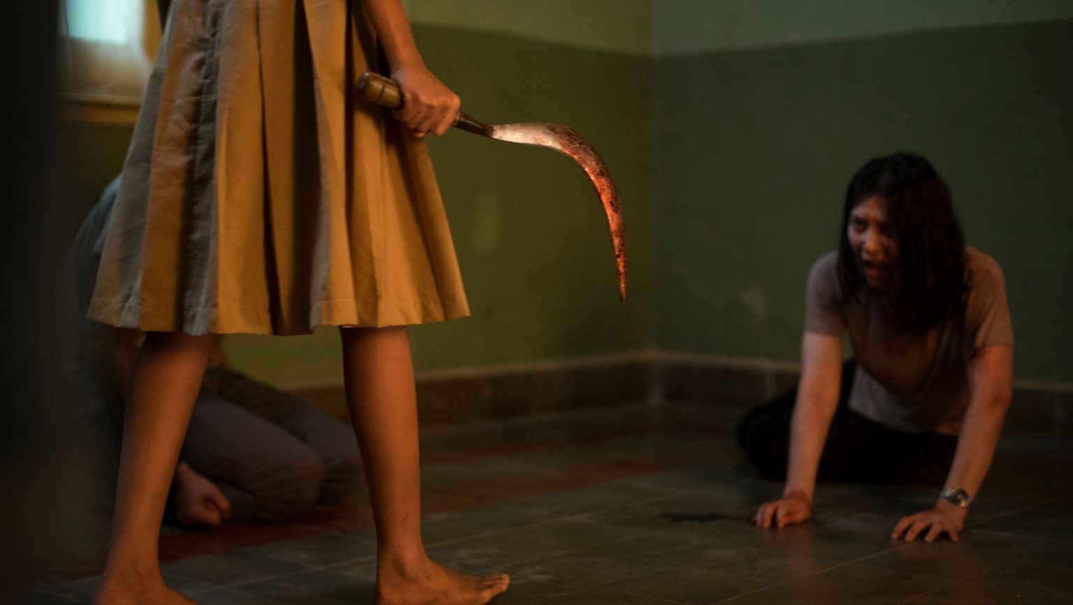 A woman looks in terror as someone in a dress approaches her with a bloody hook blade as seen in The Queen of Black Magic.