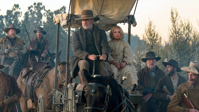 Tom Hanks and Helena Zengel ride in a horse wagon surrounded by armored guards on horses as seen in News of the World. 