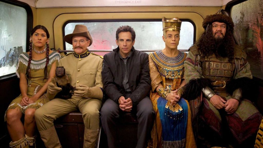 Larry Daley (Ben Stiller), Teddy Roosevelt (Robin Williams), Ahkmenrah (Rami Malek), Sacagawea (Mizuo Peck), and Atilla the Hun (Patrick Gallagher) sitting at the back of a bus in Night at the Museum: Secret of the Tomb.