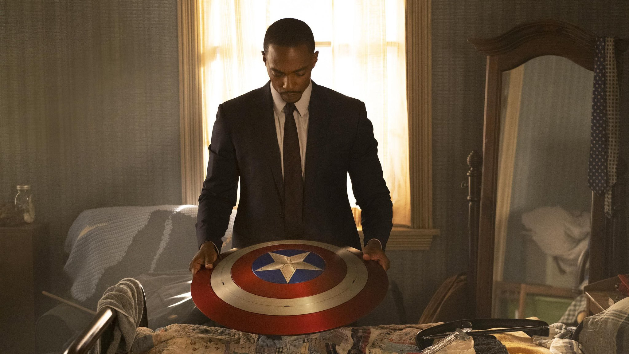 Anthony Mackie as Sam Wilson holding Captain America's shield in a suit and tie as seen in The Falcon and the Winter Soldier.