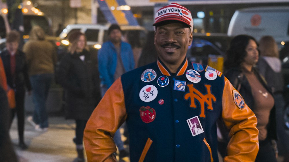 Eddie Murphy smiling and wearing a New York Mets jacket and tourist clothes as seen in Coming 2 America.