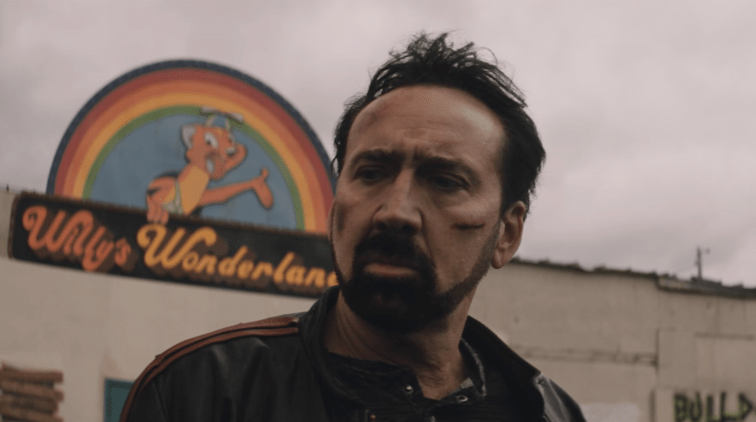 Nicolas Cage as the Janitor with battle scars standing outside of Willy's Wonderland as seen in the film directed by Kevin Lewis.