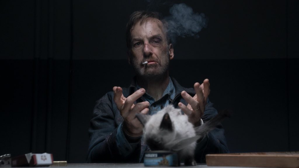 Bob Odenkirk looking beat up while smoking in front of a cat as seen in the action comedy Nobody.