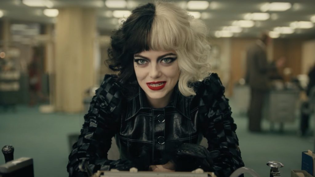 Emma Stone as Cruella sitting at a desk in a black leather outfit as seen in the new Disney live-action film.