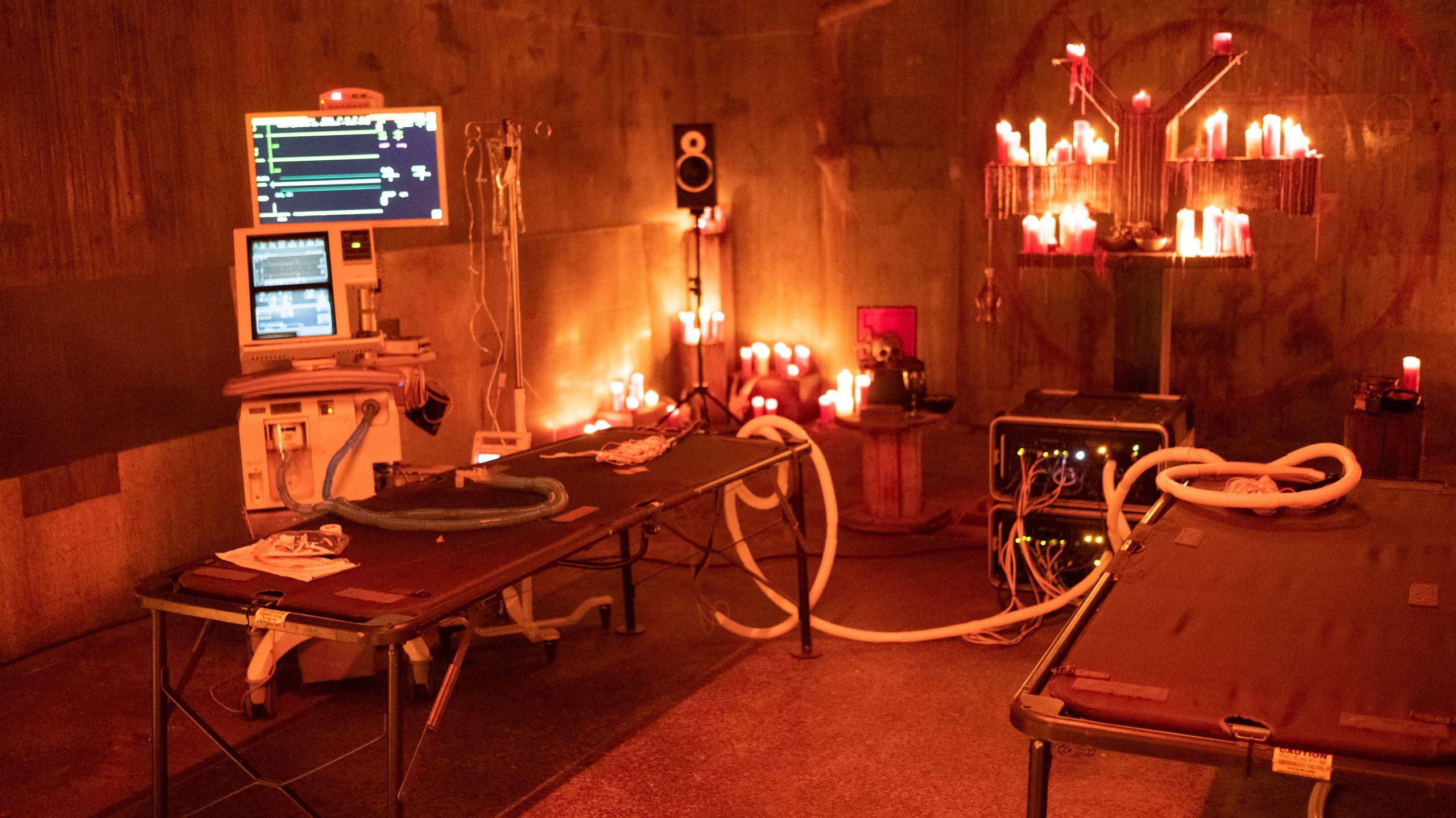 A VR set hooked up to medical supplies and anesthetics around a sinister looking chapel with burning candles and demon imagery as seen in DEMONIC directed by Neill Blomkamp. 