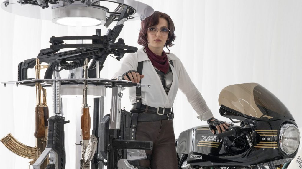 Jodie Comer as Molotov Girl next to a motorcycle and arsenal of vast machine guns as seen in the new video game action comedy FREE GUY.