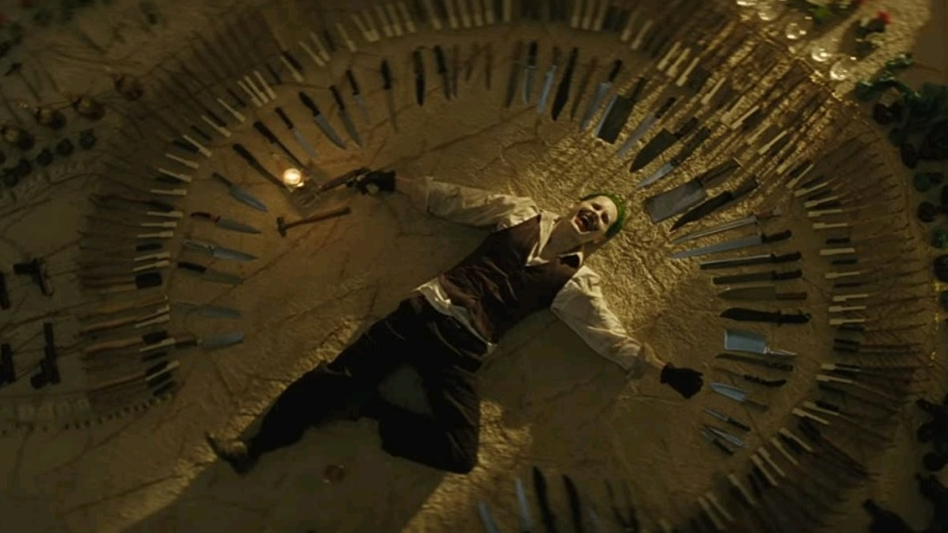 Jared Leto as the Joker laying down in a circle of sharp knives and assorted guns and weapons as seen in SUICIDE SQUAD, ranking dead last on our DCEU ranking. 