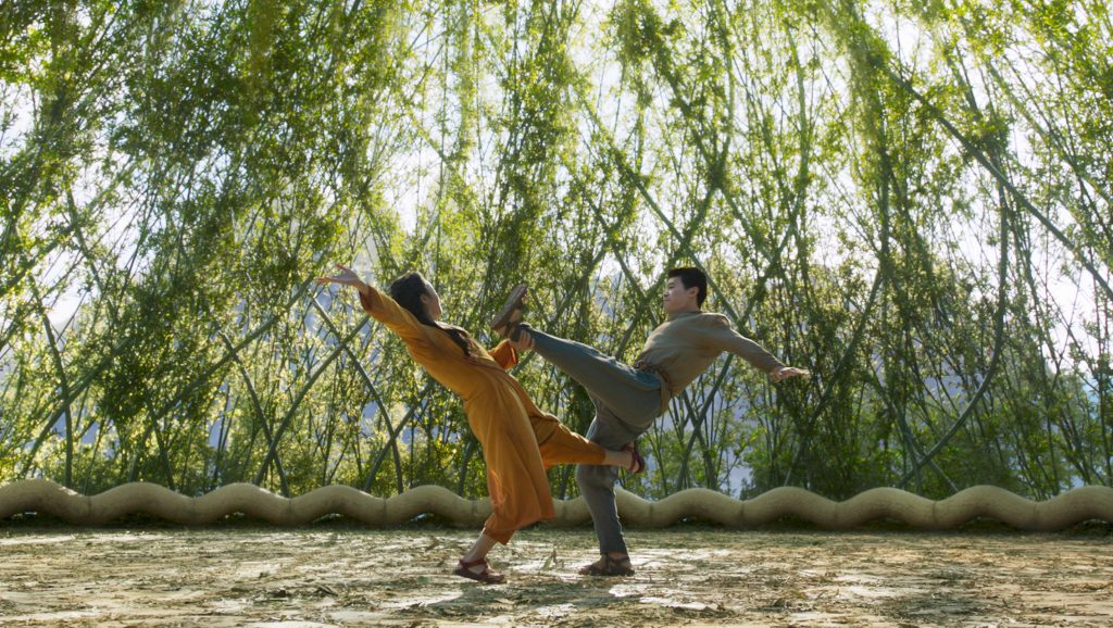 Michelle Yeoh and Simu Liu train fighting together in mid-air in a courtyard filled with green branches as seen in the new Marvel film SHANG-CHI AND THE LEGEND OF THE TEN RINGS.