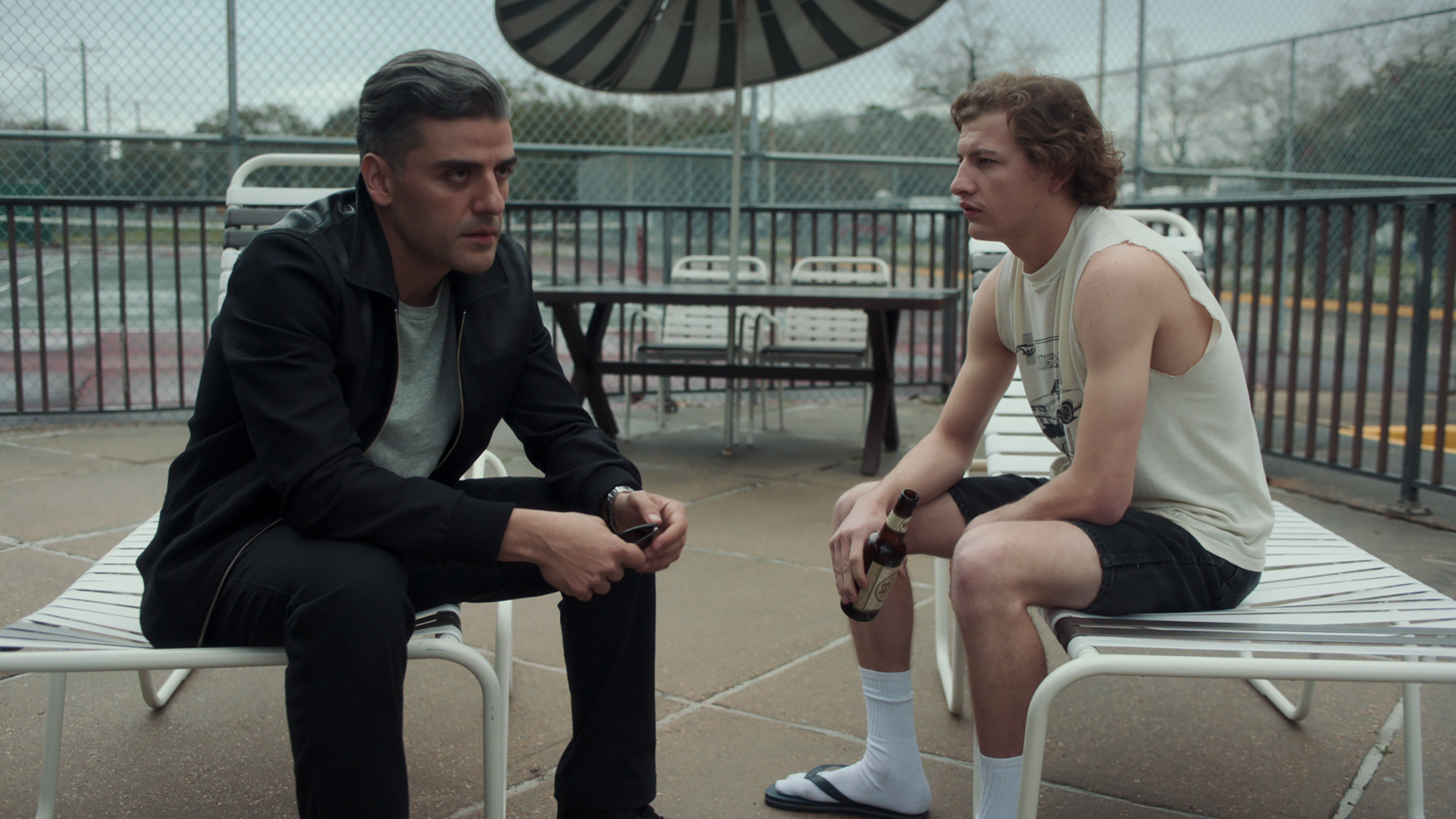 Oscar Isaac and Tye Sheridan sit together by a crummy motel pool as seen in THE CARD COUNTER directed by Paul Schrader.