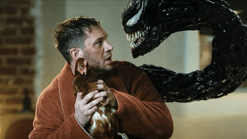 Tom Hardy holds a chicken while wearing a night robe as he's confronted by the Venom Symbiote coming out of his body in VENOM: LET THERE BE CARNAGE.