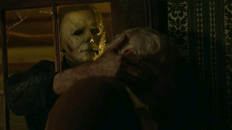 Michael Myers breaks through a glass window and grabs an elderly man from inside his home by the head as seen in HALLOWEEN KILLS.