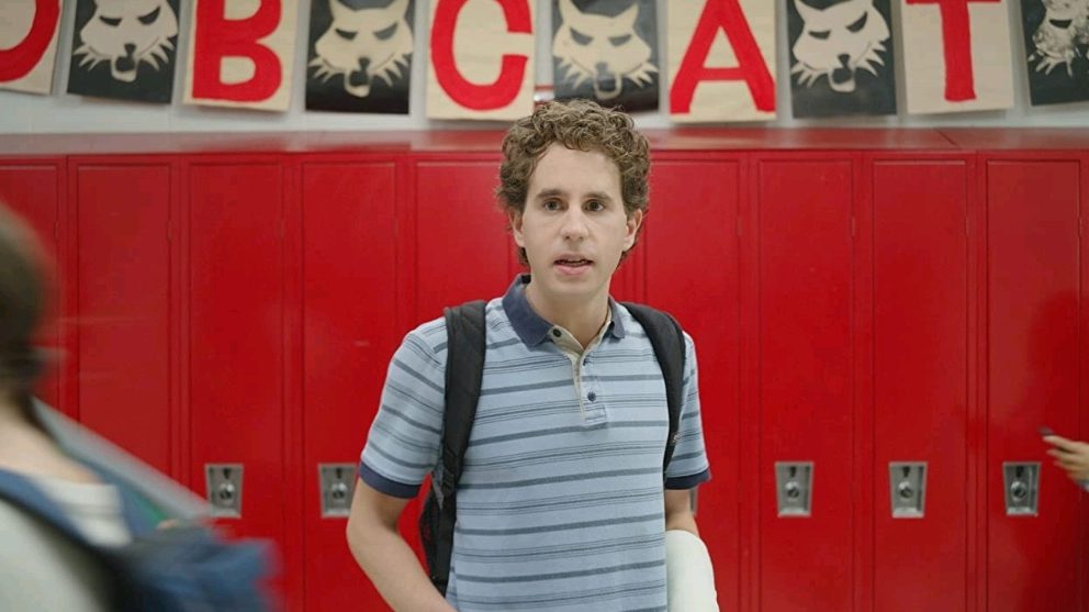 Ben Platt stands in a busy high school hallway in front of some bright red lockers with decorations that read "Go Bobcats" in DEAR EVAN HANSEN.