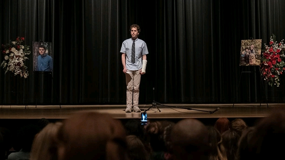Ben Platt stands alone on a dark high school stage for a memoriam speech in DEAR EVAN HANSEN.