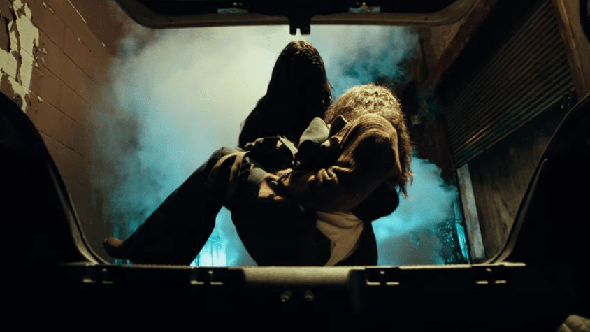 Gabriel the mysterious demonic killer dressed in black leather puts a female victim in a trunk as seen in MALIGNANT directed by James Wan.