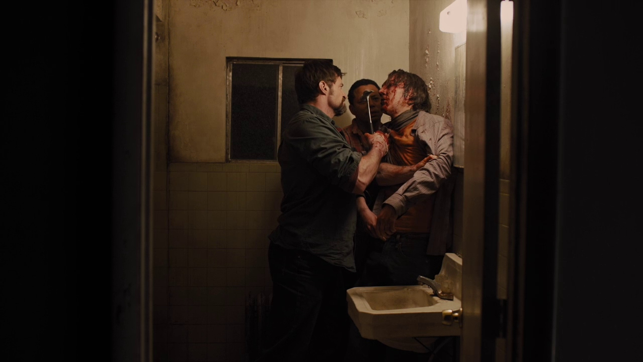 Hugh Jackman holds a bloody and beaten Paul Dano up to a rusted bathroom wall with a hammer as seen in PRISONERS directed by Denis Villeneuve.