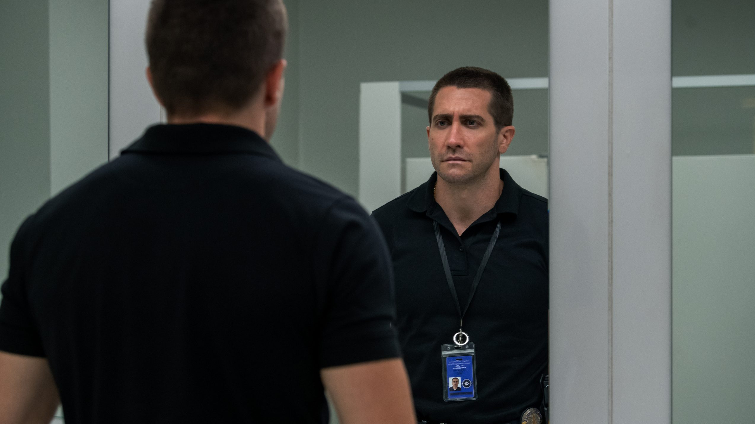 Jake Gyllenhaal questions his morale in the mirror while wearing his 911 operator badge as seen in THE GUILTY directed by Antoine Fuqua. 
