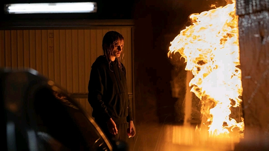 Agathe Rousselle as Alexia starring at a huge wave of fire in a car garage in TITANE directed by Julia Ducournau.