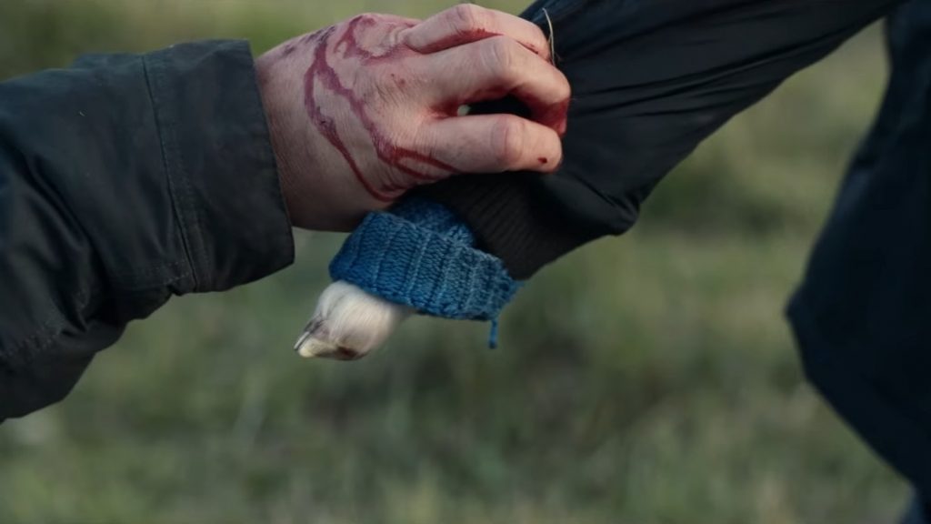 A bloody adult hand holds the hoof arm of Ada the half-human, half-sheep hybrid child in desperation as she walks away as seen in the new A24 horror film LAMB.