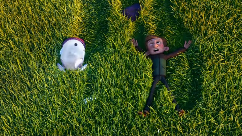 Barney, voiced by Jack Dylan Grazer, and Ron the little blue android, voiced by Zach Galifianakis, roll down a grassy hill in laughter as seen in the new animated film RON'S GONE WRONG.
