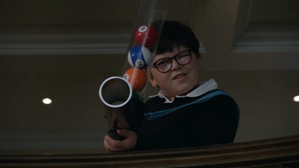 Archie Yates as mischievous young Max mercer firing a gun loaded with colorful billiards balls in the new Disney+ Home Alone sequel HOME SWEET HOME ALONE directed by Dan Mazer.