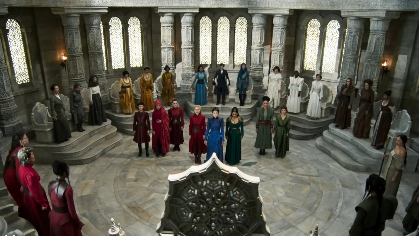 Rosamund Pike as Moiraine Damodred stands in the center of a great white throne room surrounded by other colorful factions of leaders as seen in the Amazon Prime Video adaptation of THE WHEEL OF TIME.  
