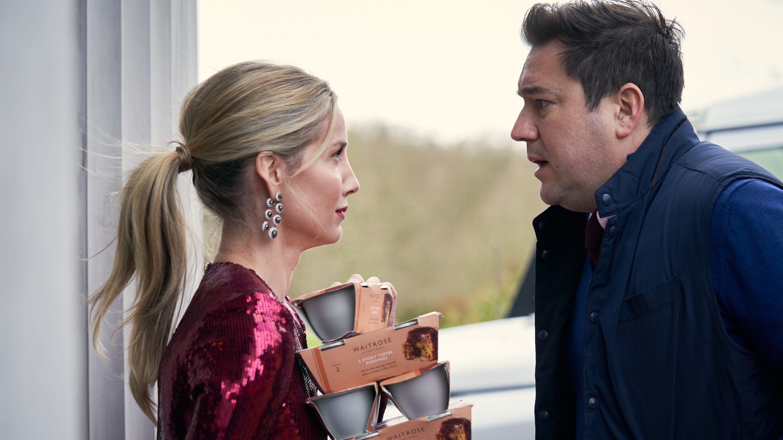 Annabelle Wallis and Rufus Jones stare at each other awkwardly as they bring in groceries to a seemingly normal holiday get together as seen in the dark comedy SILENT NIGHT. 