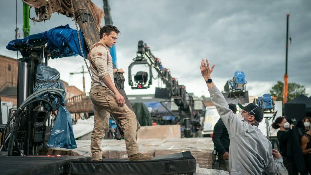 Director Ruben Fleischer frames a huge action shot of Tom Holland in costume as Nathan Drake on the stunt set of UNCHARTED.