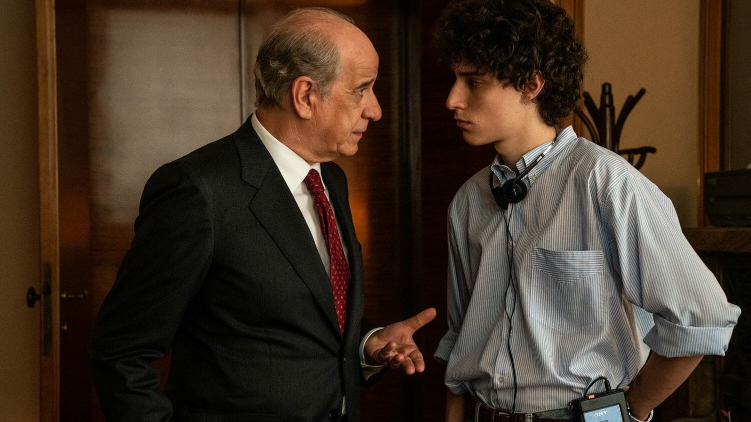 Toni Servillo wearing a business suit lectures Filippo Scotti with a Sony walkman around his neck in THE HAND OF GOD on Netflix, nominated for Best International Feature at the 2022 Oscars.