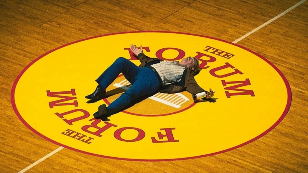 John C. Reilly as Lakers owner Jerry Buss laying down in the middle of the famous Forum Arena basketball court with a bottle of champagne in hand as seen in WINNING TIME: THE RISE OF THE LAKERS DYNASTY on HBO. 