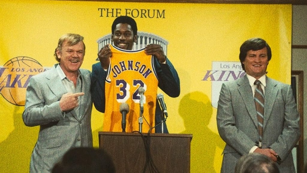 John C. Reilly as Jerry Buss and Jason Clarke as Jerry West welcome Earvin "Magic" Johnson played by Quincy Isaiah to the Los Angeles Lakers while showing off his iconic number 32 gold and purple jersey at the famous Forum arena in WINNING TIME: THE RISE OF THE LAKERS DYNASTY on HBO.