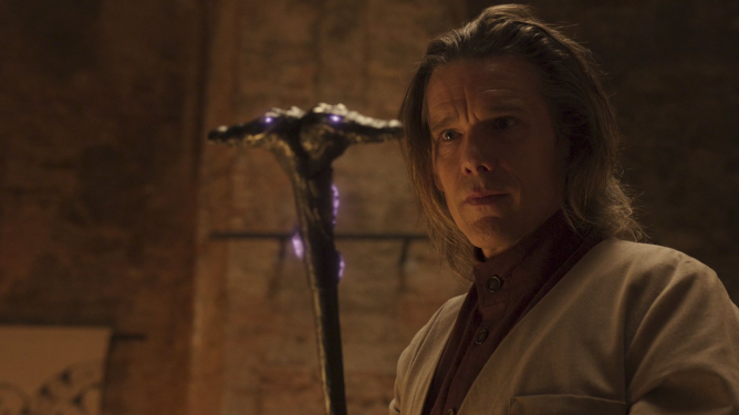 Ethan Hawke as Arthur Harrow stares at his purple glowing staff shaped by two crocodile heads facing opposite directions in the MCU Disney+ series MOON KNIGHT.