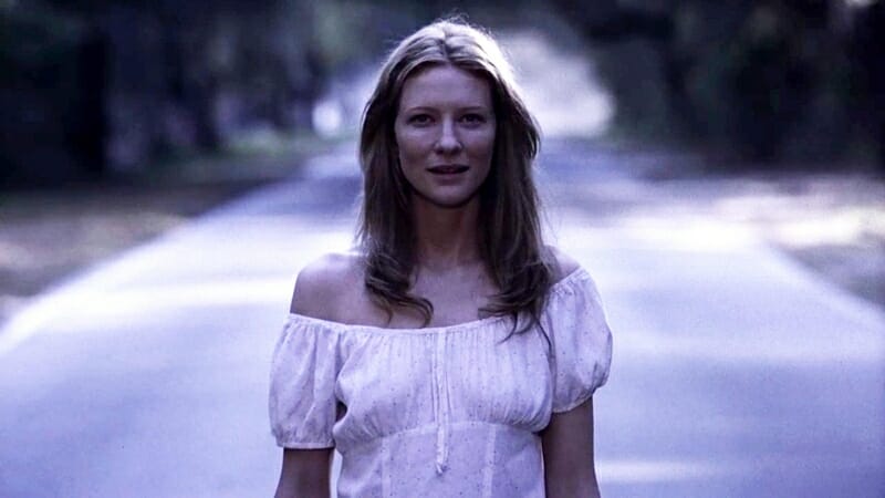 Cate Blanchett walks down the middle of an empty road in a dreamlike state while wearing a white gown in THE GIFT directed by Sam Raimi. 