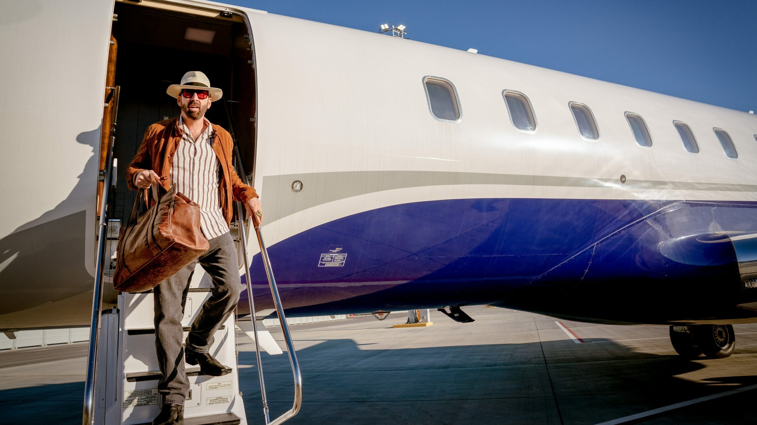 Nicolas Cage exits a private jet wearing red sunglasses and a cowboy hat on his way to his number one fan's birthday party in THE UNBEARABLE WEIGHT OF MASSIVE TALENT.