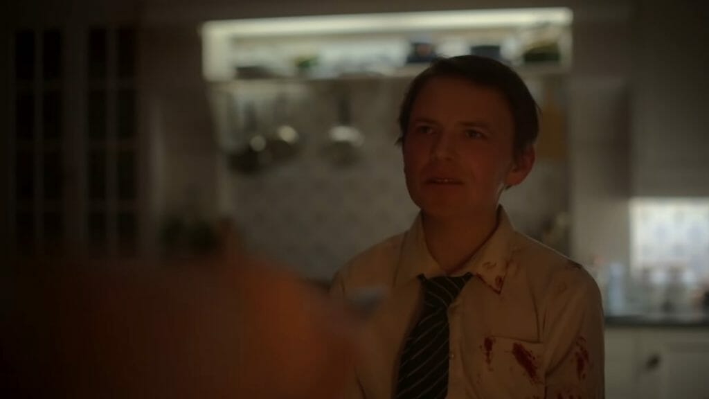 Rory Kinnear's de-aged face appears on the body of a young boy wearing a blood stained school uniform as he attempts to attack Jesse Buckley who holds him at knife point in the A24 arthouse horror film MEN.
