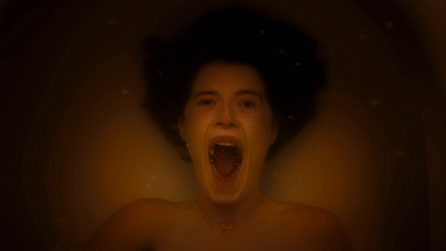 Jesse Buckley yells in terror with her mouth wide open while she drowns underwater in a bathtub naked in the A24 arthouse horror film MEN directed by Alex Garland.