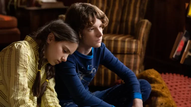 Siblings Finney and Gwen played by Mason Thames and Madeleine McGraw lean on each other in sadness in their 1970s living room in the new horror film THE BLACK PHONE. 