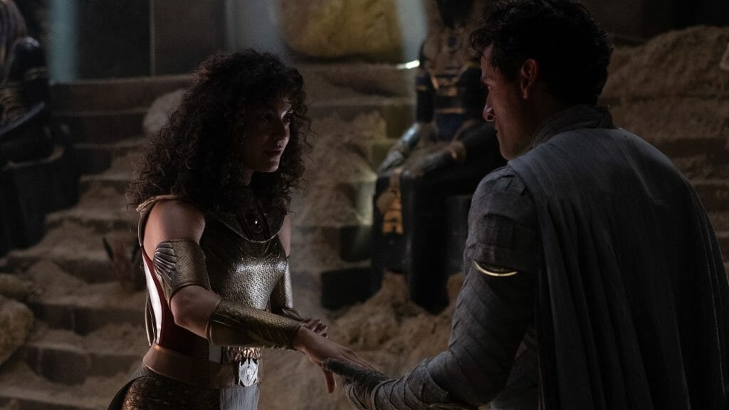 May Calamawy holds hands with Oscar Isaac as Moon Knight in her shiny golden and white Scarlet Scarab armor on the battlefield in the MCU series MOON KNIGHT on Disney+.