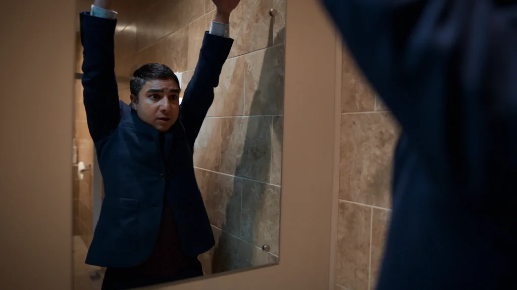 Nate played by Nick Mohammed stands nervously in a restroom with his arms up in the air and dress suit on backwards in TED LASSO Season 2 on AppleTV+.