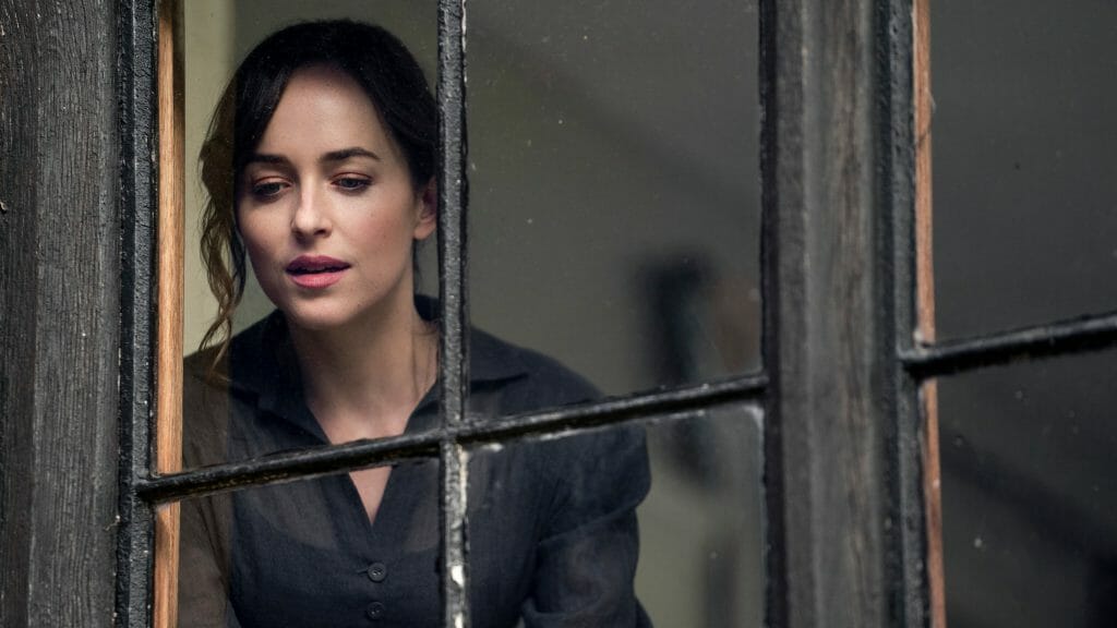 Dakota Johnson as Anne Elliot stares out of a large window in glee and wonder as seen in the 2022 Netflix adaptation of the classic Jane Austen novel PERSUASION.