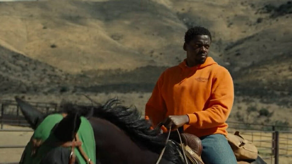 Daniel Kaluuya rides a horse wearing an orange Scorpion King crew sweater in Jordan Peele's NOPE.