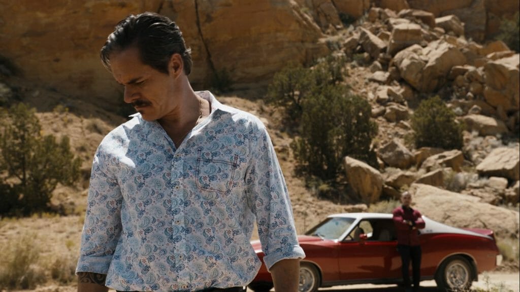 Tony Dalton as Lalo Salamanca staring down at the desert dirt while Nacho stands far behind him next to a red sports car in the BETTER CALL SAUL episode titled Bad Choice Road. 