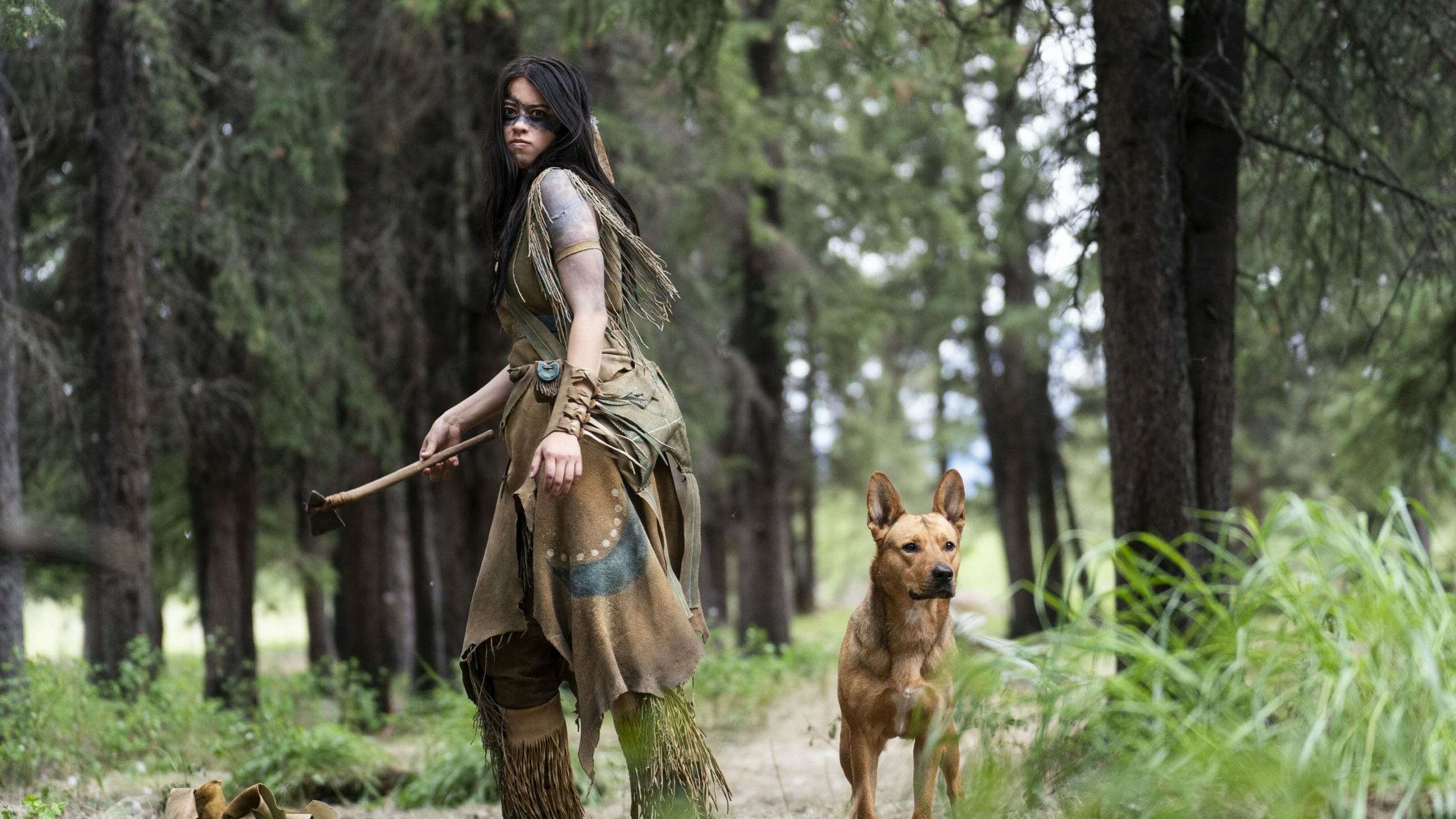 Amber Midthunder as the Comanche warrior Naru holds her tomahawk next to her loyal dog named Sarii in PREY now streaming on Hulu. 