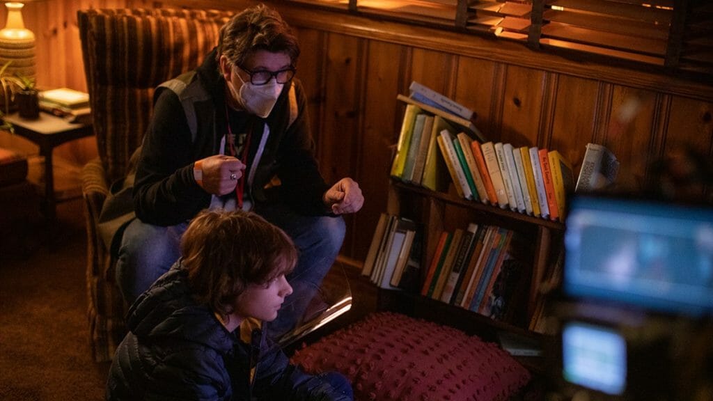 Director Scott Derrickson walks young actor Mason Thames through a scene where he's watching TV in an old 1970s living room from the behind the scenes of THE BLACK PHONE.