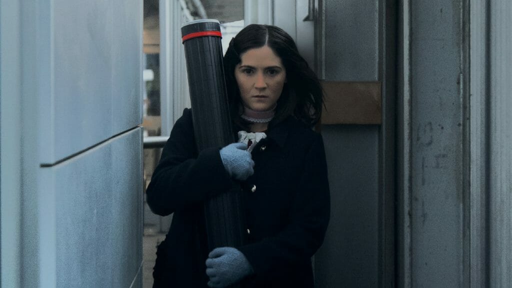 Esther played by Isabelle Fuhrman walks down an empty hallway holding supplies with an evil sinister look in the horror prequel ORPHAN: FIRST KILL.