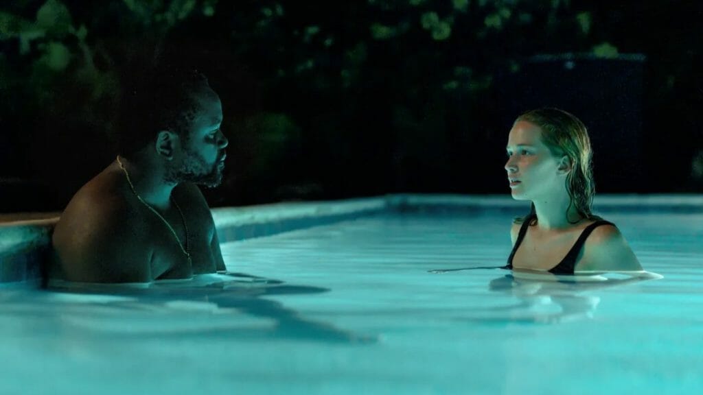 Brian Tyree Henry and Jennifer Lawrence share a quiet moment of platonic intimacy standing together in a pool in the film CAUSEWAY on AppleTV+. 