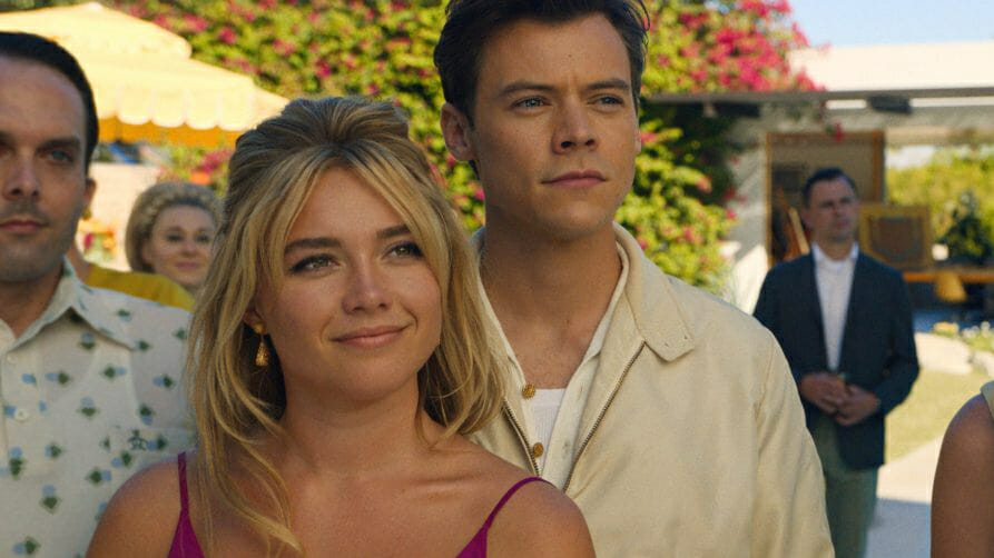 Florence Pugh and Harry Styles pose together happily at a garden dinner party in the dystopian suburban town of Victory in DON'T WORRY DARLING. 