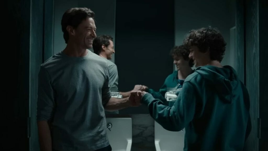 Hugh Jackman bumps fists with his teenage boy played by Zen McGrath in front of their bathroom mirror in THE SON directed by Florian Zeller. 